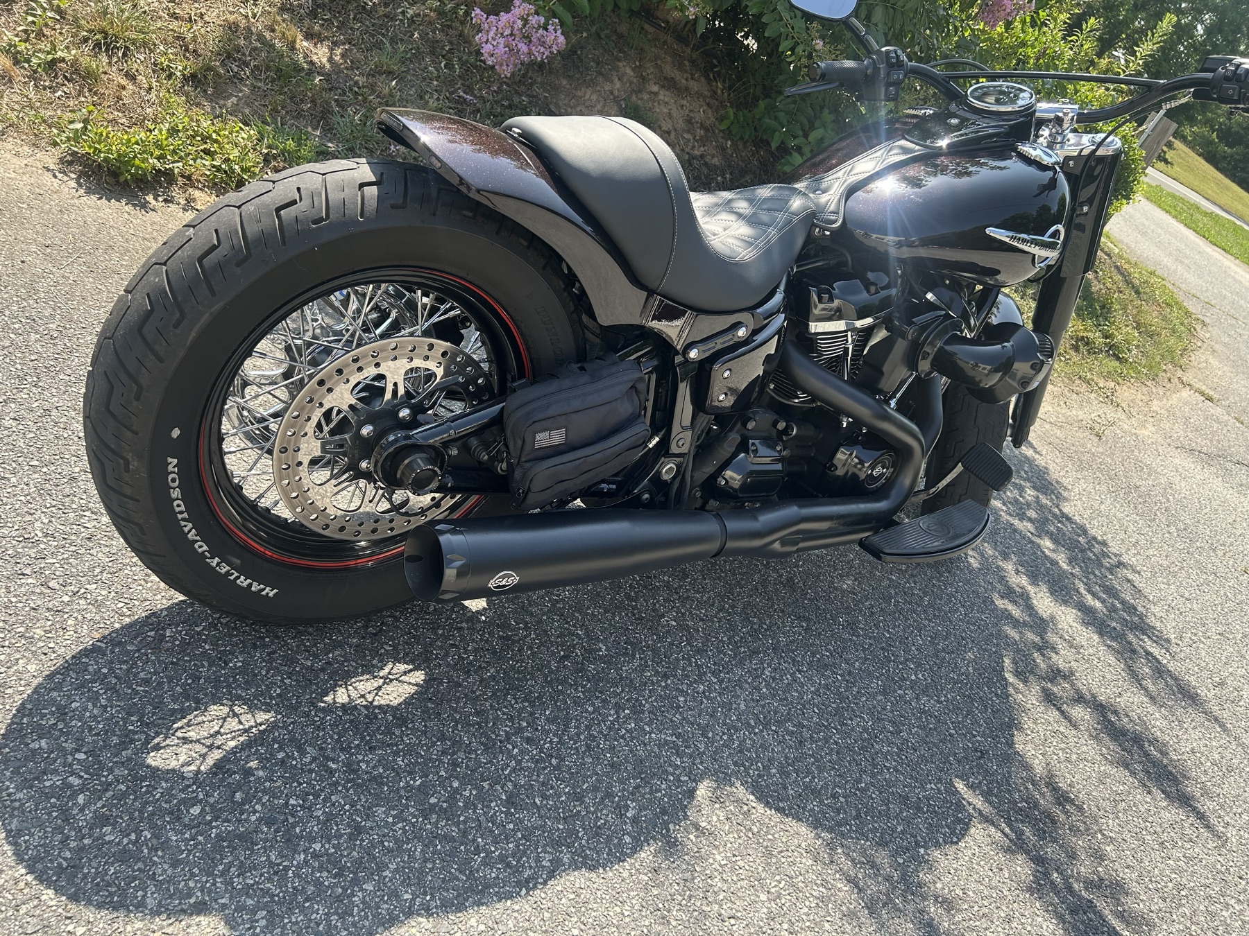 Blacked-out Harley-Davidson bobber with laced wheels and whitewall-lettered tires, rear three-quarter view outside the shop